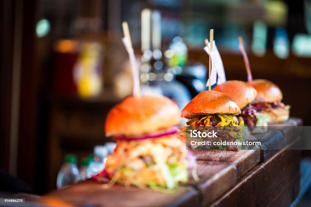 Close up image of a selection of freshly flame grilled burgers in a row on a wooden counter at Borough Market, one of the oldest and most famous food markets in the world. Each of the burgers has its own label, on which is written the contents of the burger. The burgers are sandwiched between glazed buns, and presented on beds of fresh green lettuce and stuffed with melted cheese and red onion. Horizontal colour image with copy space.